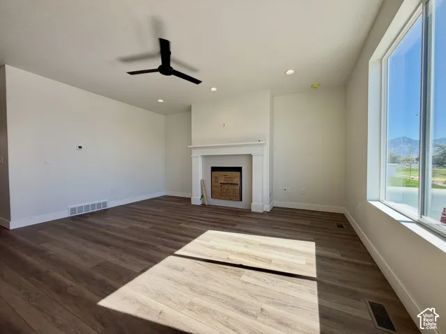 Spacious room featuring wood-finish flooring, a contemporary ceiling fan, recessed lighting, a fireplace with a white mantel, and large windows