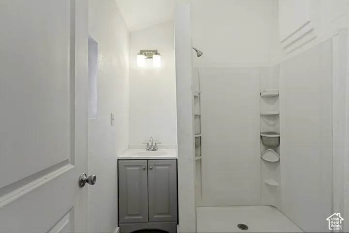 Shower with integrated shelving, a single vanity with storage, and wall-mounted lighting