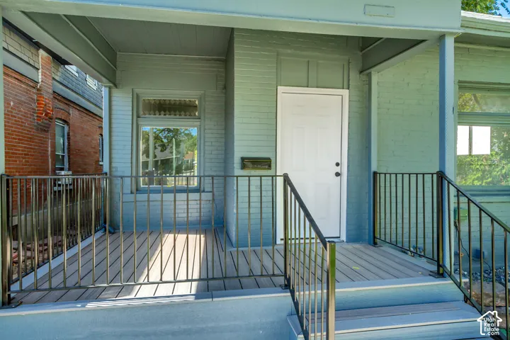 Covered front porch featuring composite decking, black metal railings, and a white paneled entry door