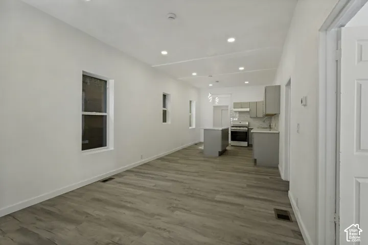 Open-concept living space featuring wood-finish flooring, recessed lighting, and a kitchen with gray cabinetry, a range, and a central island