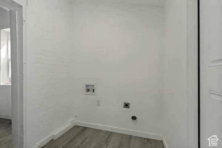 Laundry area with wood-finish flooring and white walls, featuring a utility box with plumbing hookups and a dryer vent