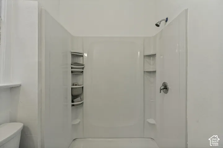 White shower enclosure with a chrome shower head and built-in shelving