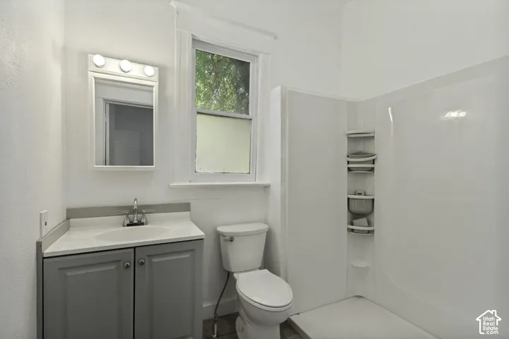 White solid surface vanity with undermount sink, gray cabinetry, and a mirrored medicine cabinet with integrated lighting