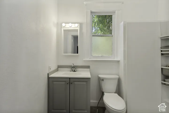 Bathroom featuring a window, vanity with gray cabinetry, integrated sink, and wall-mounted mirror with lighting
