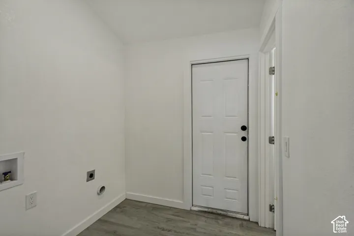 Dedicated laundry space featuring wood-finish flooring, white walls, and a paneled entry door
