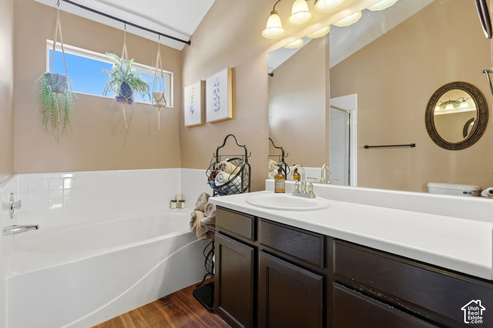 White bathtub with tile surround, wood-finish flooring, dark wood-finish vanity, white countertop, and wall-mounted mirror