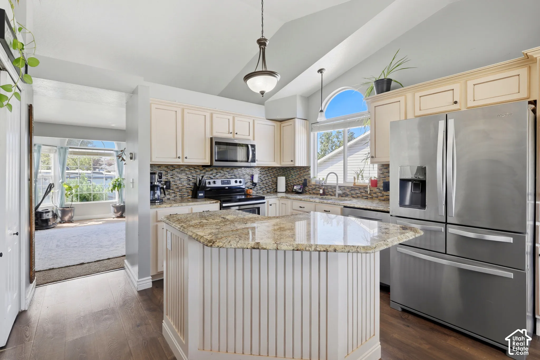 Vaulted ceiling with an arched window, stainless steel appliances, wood-finish flooring, light-toned cabinetry, and a kitchen island with a stone countertop