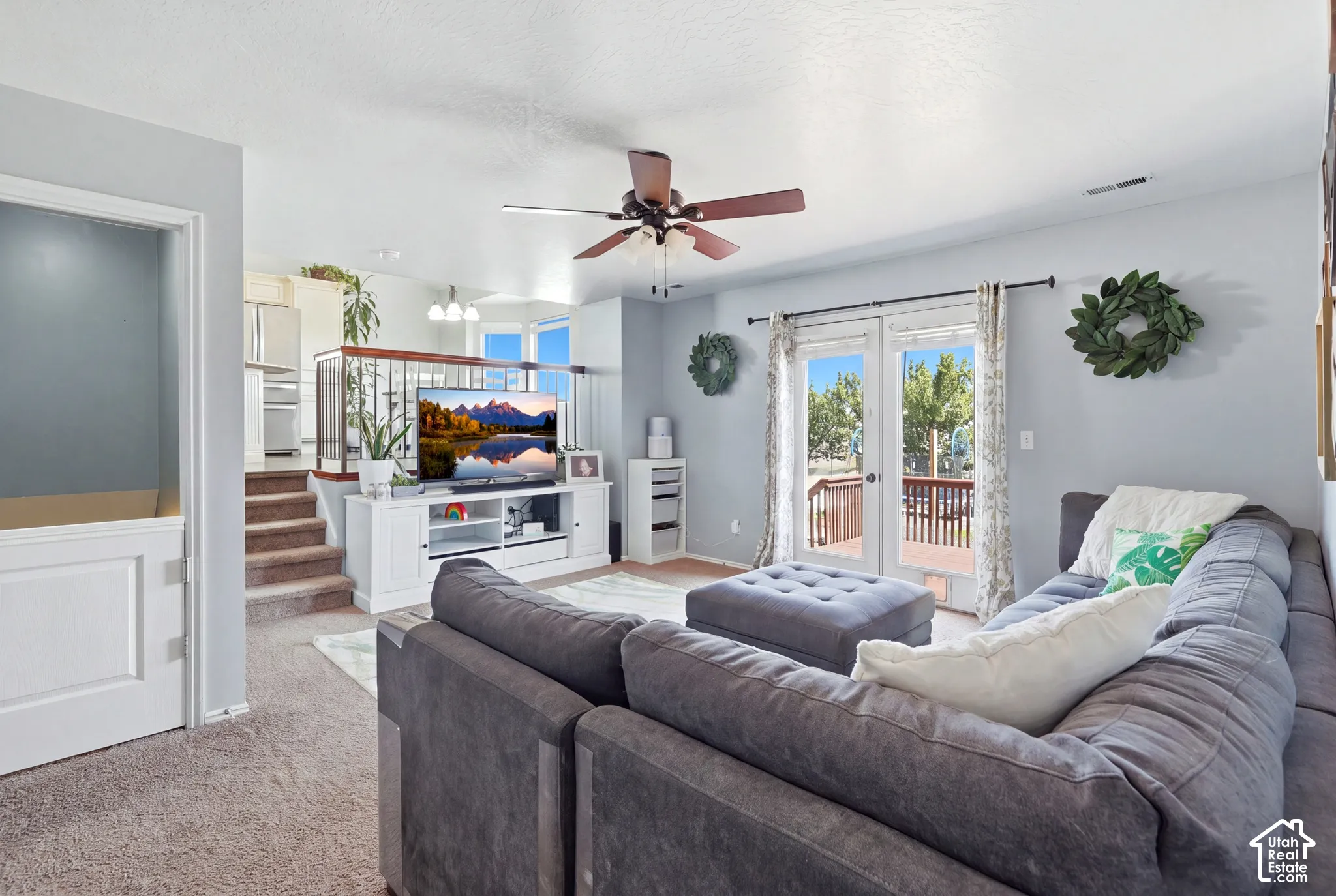 Light-toned carpeted flooring, French doors opening to an exterior deck, a ceiling fan with integrated lighting, and a built-in media console
