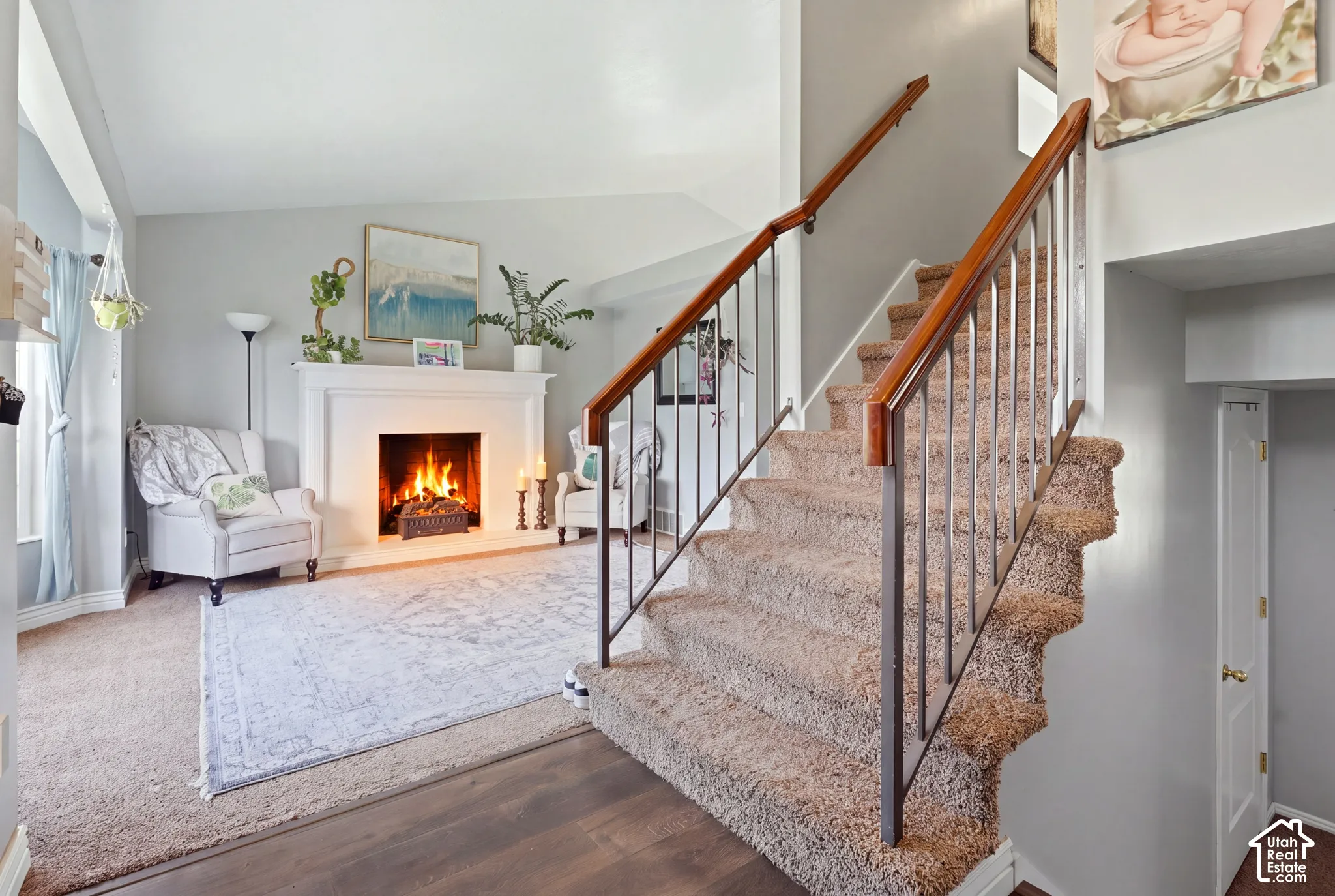Spacious living area featuring a fireplace with a white mantel, wood-finish flooring, and carpeted stairs with a wood and metal railing