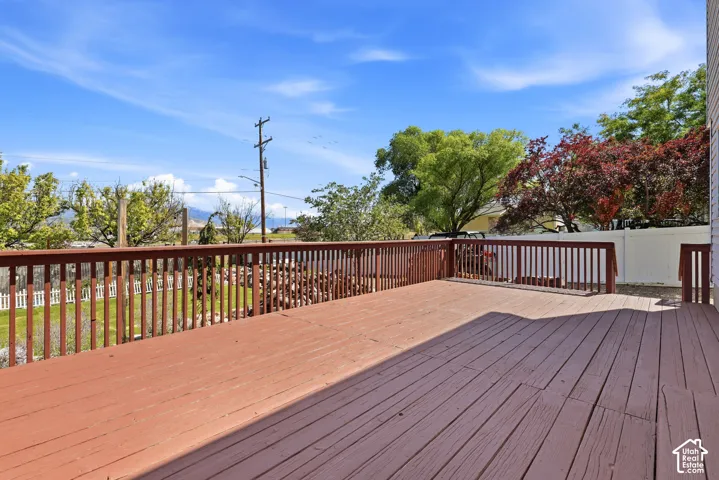 Expansive outdoor deck with wood railing, featuring a privacy fence and mature trees