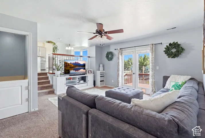 Light-toned carpeted flooring, French doors opening to an exterior deck, a ceiling fan with integrated lighting, and a built-in media console