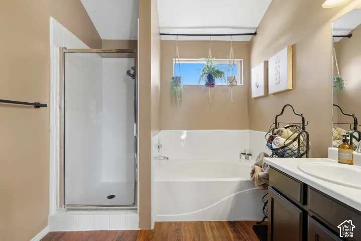 Wood-finish flooring, built-in bathtub, glass-enclosed shower, wall-mounted mirror, and vanity with integrated sink