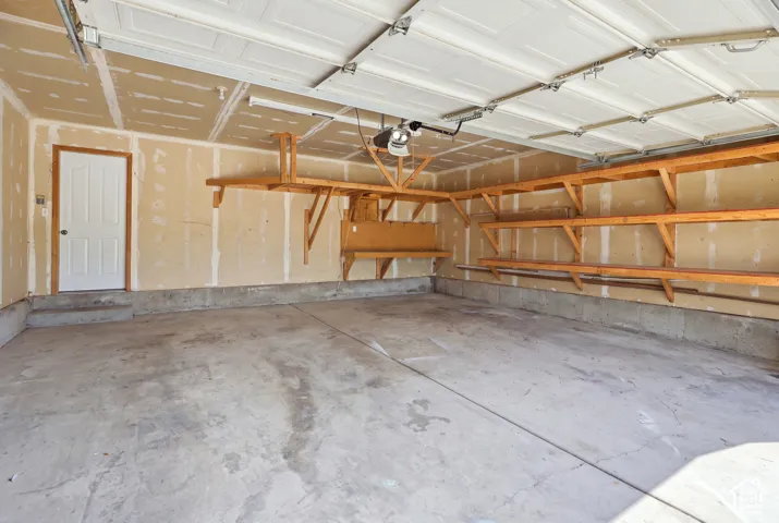 Spacious garage with concrete flooring, built-in wooden shelving, and an overhead door