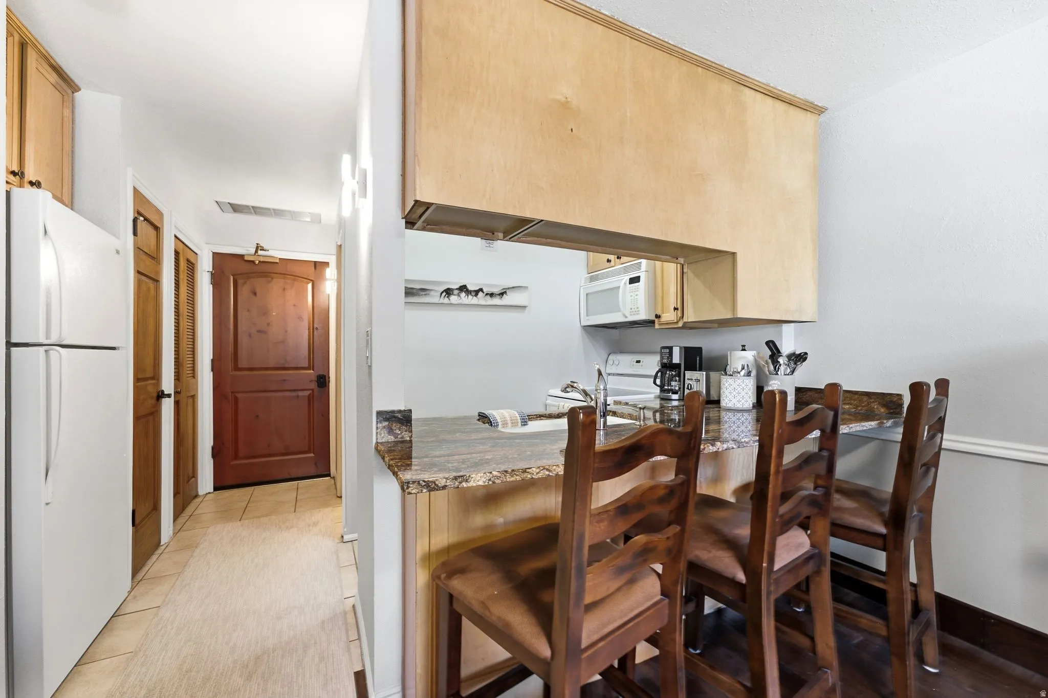 Kitchenette with wood-finish cabinetry, granite-style countertops, integrated stainless steel microwave, and a white refrigerator