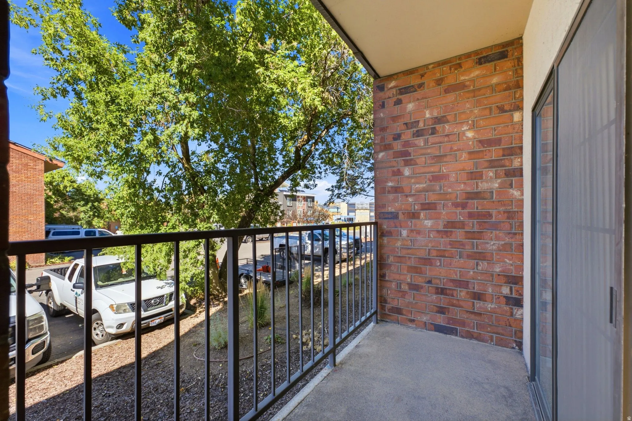 Outdoor balcony with brick-finish exterior, concrete flooring, and metal railing