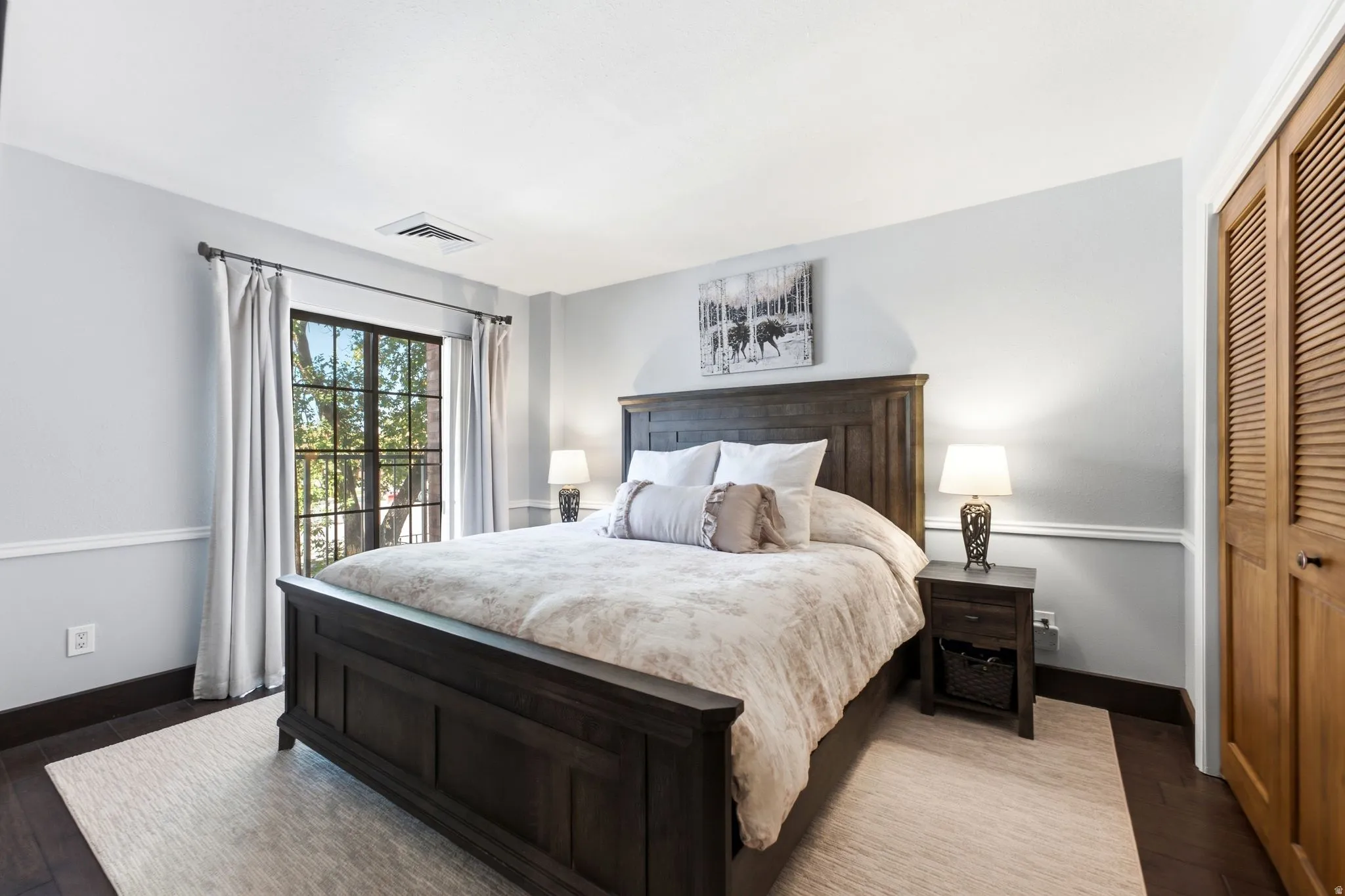 Spacious room featuring wood-finish flooring, a large window with black grilles, and louvered bifold closet doors