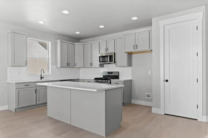 Modern kitchen featuring light gray cabinetry, white countertops, stainless steel appliances, a center island, and wood-finish flooring