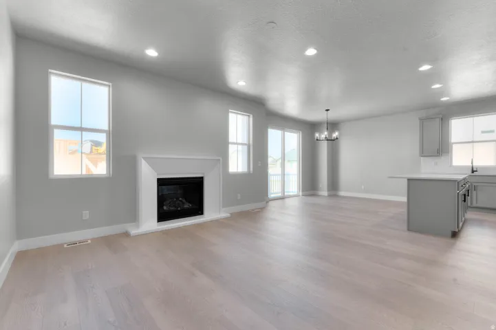 Spacious open concept living area featuring a fireplace with a white mantel, numerous recessed lights, wood-finish flooring, and sliding glass doors to the exterior
