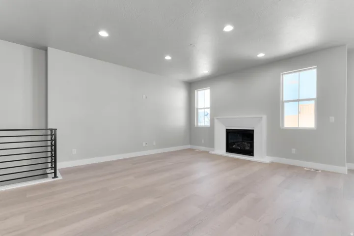 Spacious room featuring wood-finish flooring, a fireplace with a white surround, and recessed lighting