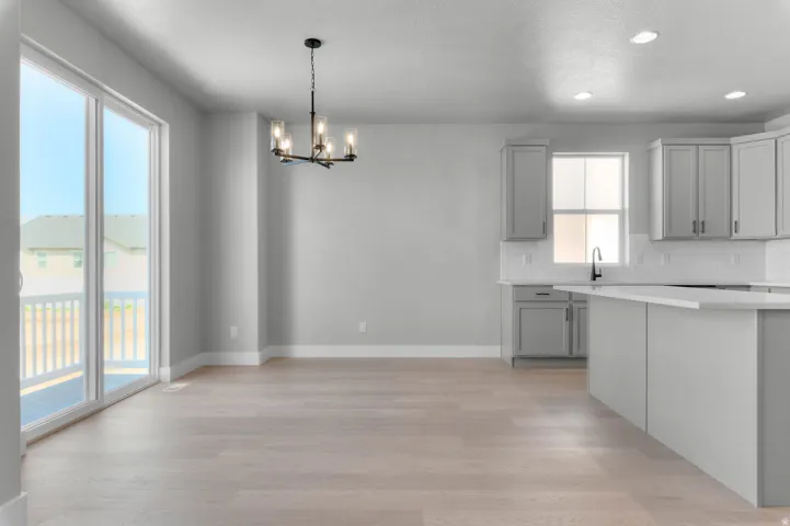 Wood-finish flooring throughout, sliding glass door with balcony access, modern chandelier, recessed lighting, and gray cabinetry with white countertops