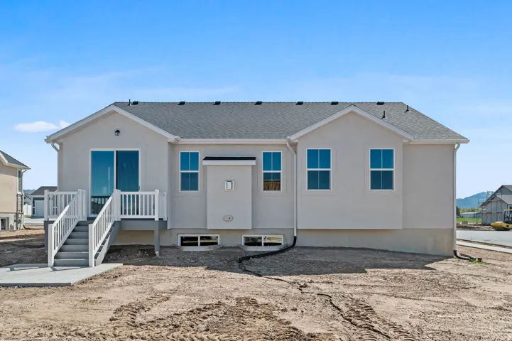 Rear exterior with light-toned stucco, a dark shingled roof, a white deck with railings, and sliding glass door access