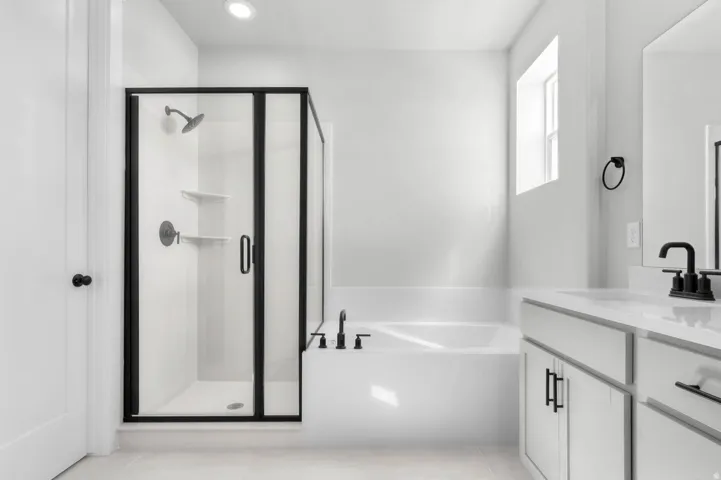 Spacious bathroom featuring a glass-enclosed shower with matte black fixtures, a built-in tub, dual vanity with a light-toned countertop, and recessed lighting