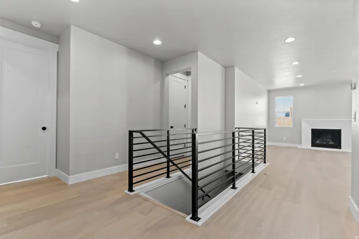Recessed lighting, wood-finish flooring, contemporary black metal railing, and a fireplace with a white mantel