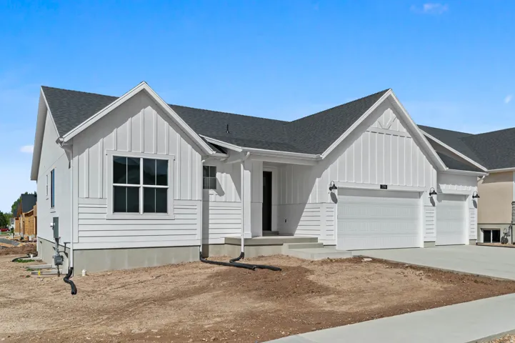 White exterior siding with board and batten accents, dark asphalt shingle roof, two garage bays with white doors, and black outdoor sconce lighting
