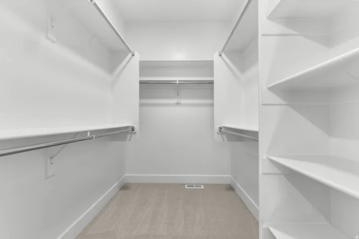 Built-in shelving, multiple hanging rods, white walls, and light-colored carpeting