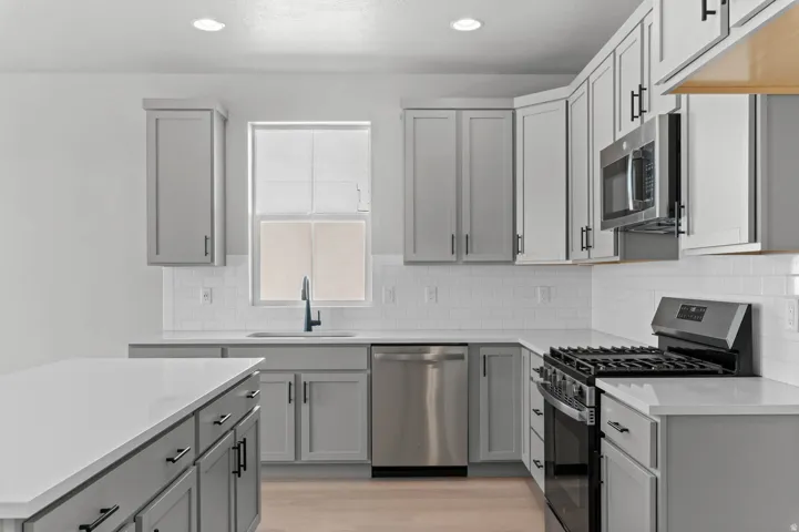 Kitchen featuring light gray cabinetry, white countertops, stainless steel appliances, white subway tile backsplash, and wood-finish flooring