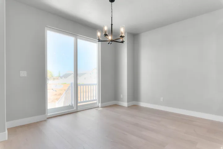 Wood-finish flooring, sliding glass door, white trim, and a black metal chandelier with clear glass shades