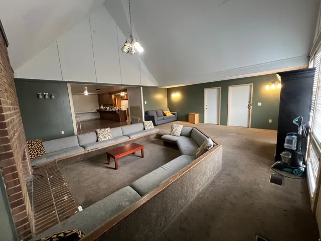 Vaulted ceiling with exposed beams, brick accent wall, recessed seating area, and overhead lighting