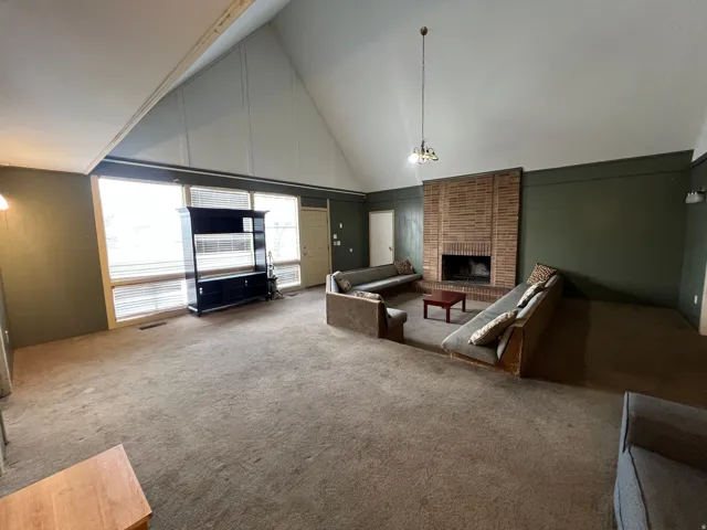 Vaulted ceiling with exposed beam, brick-clad fireplace, and expansive windows
