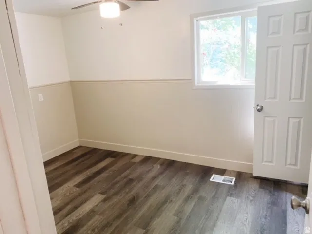Wood-finish flooring, white trim, ceiling fan with light fixture, and a paneled interior door