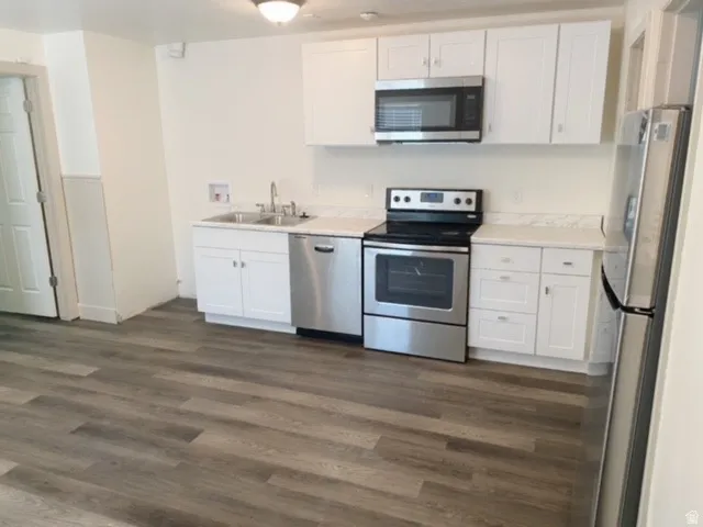 Kitchen featuring white cabinetry, wood-finish flooring, stainless steel appliances, a double basin sink, and light-toned countertops
