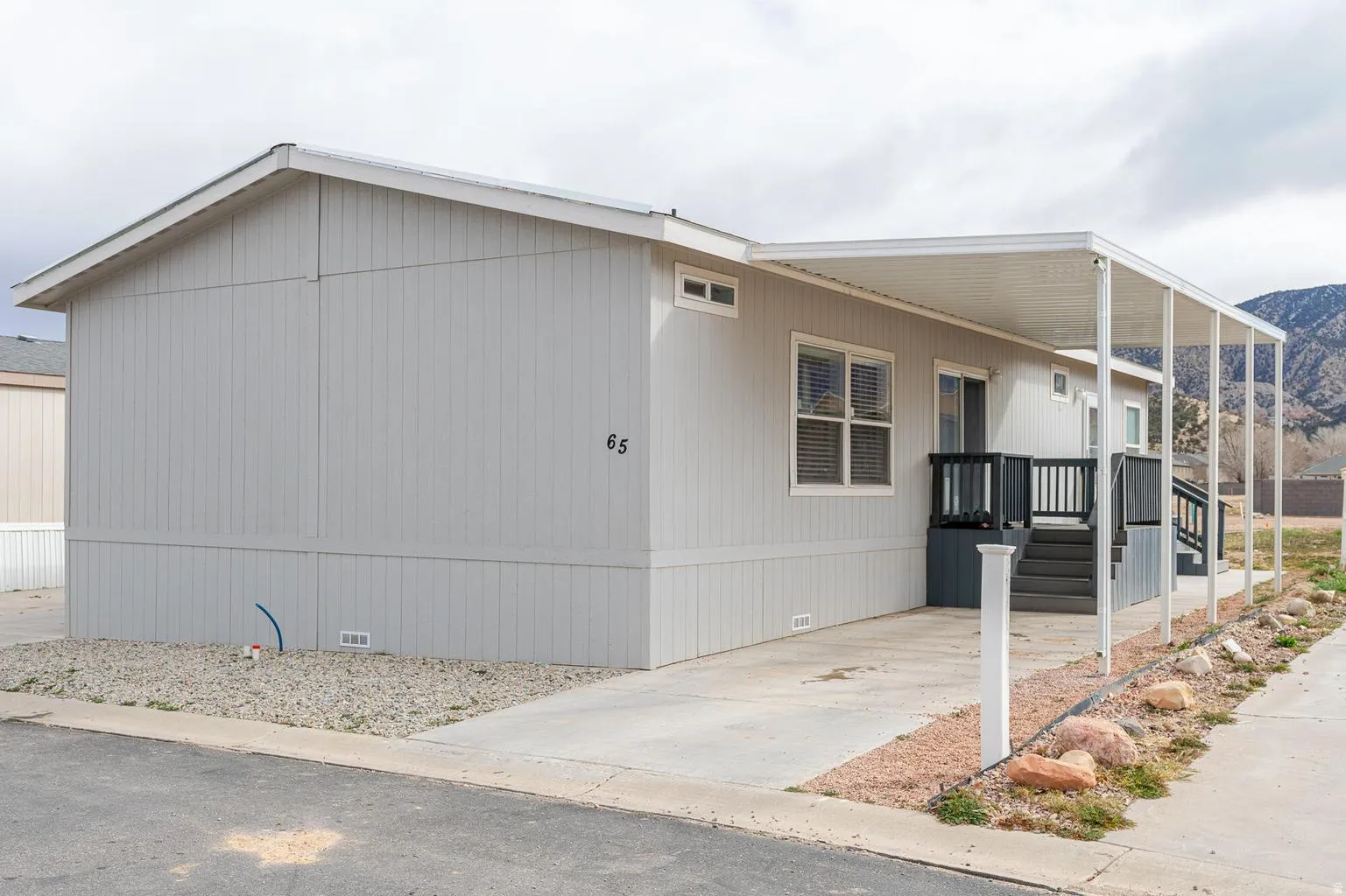 Light grey siding with white trim, covered patio, dark grey porch, gravel landscaping, paved parking