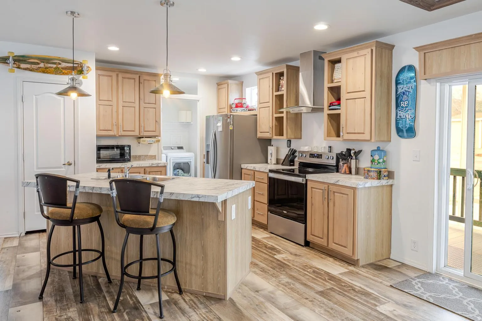 Kitchen featuring wood-finish flooring, light wood cabinetry, a center island with countertop seating, stainless steel appliances, and recessed lighting