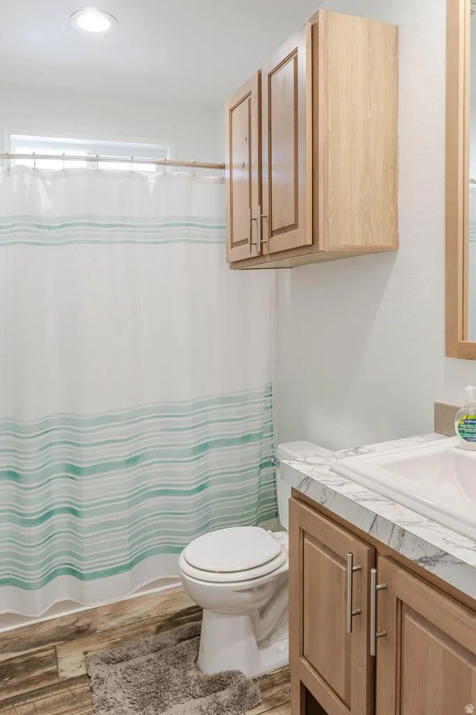 Recessed ceiling lighting, wood-finish flooring, light wood tone cabinetry, vanity with integrated sink, and a window for natural light