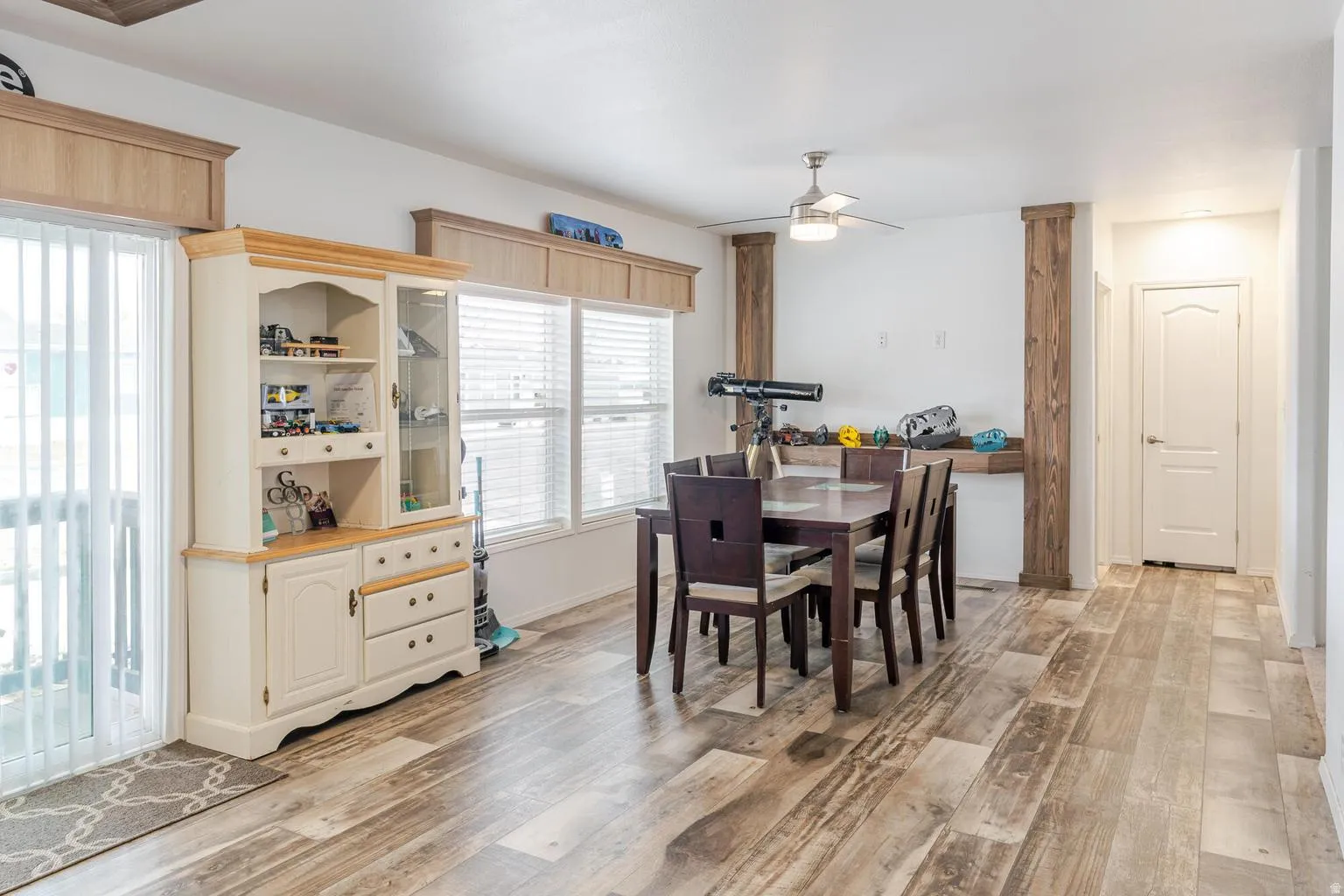 Wood-finish flooring throughout, multiple windows with blinds, sliding glass door, ceiling fan with light fixture, and white interior doors