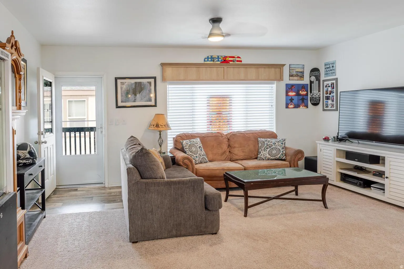 Living area featuring a ceiling fan, window with blinds, wood-finish flooring, and light-colored carpet