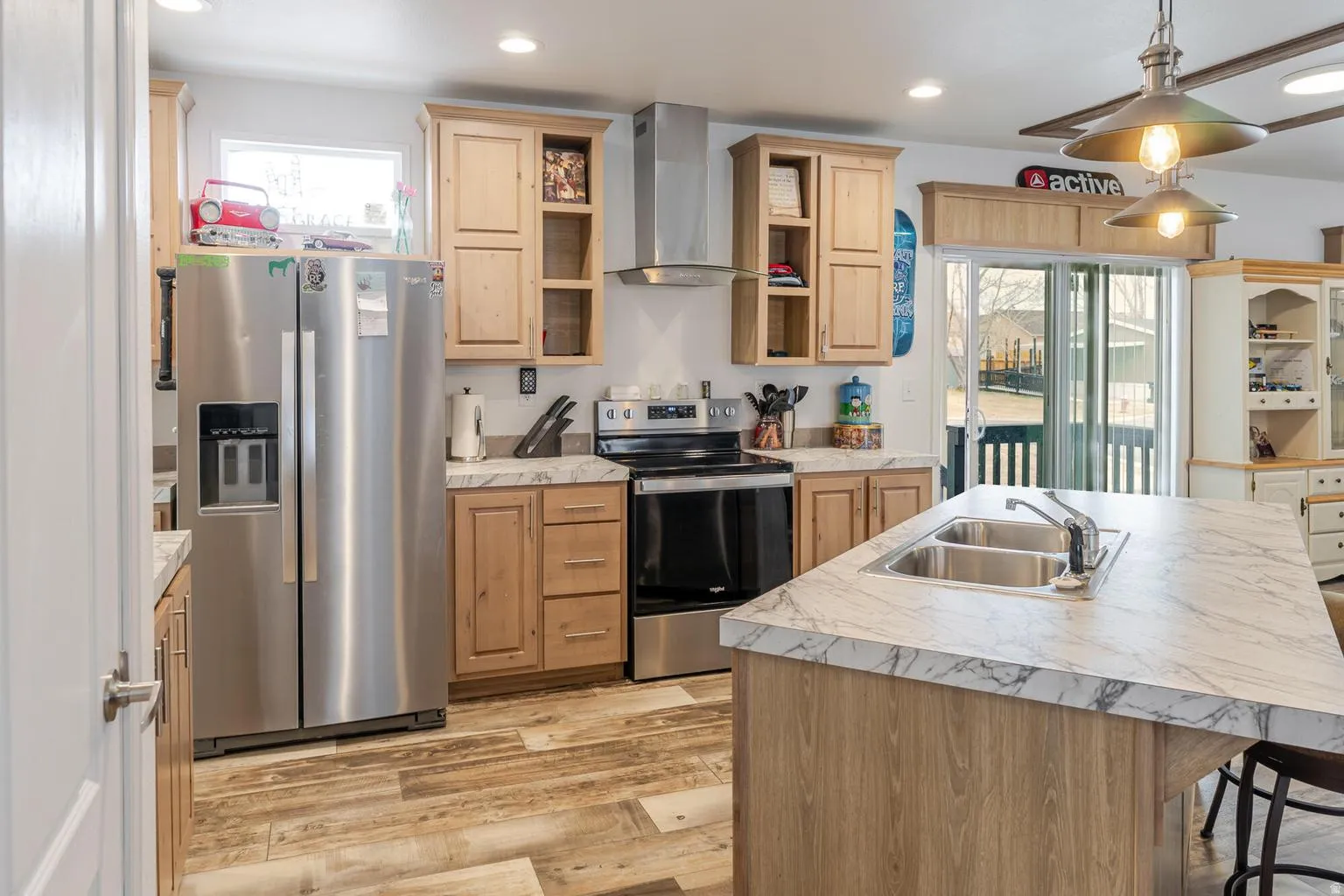 Kitchen featuring wood-finish cabinetry, stainless steel appliances, a center island with a double basin sink, and wood-finish flooring