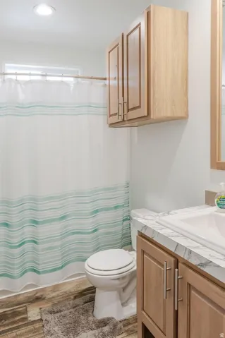 Recessed ceiling lighting, wood-finish flooring, light wood tone cabinetry, vanity with integrated sink, and a window for natural light
