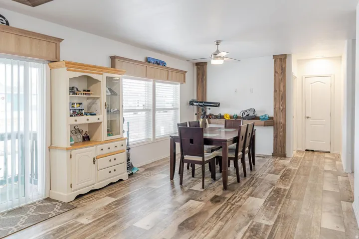 Wood-finish flooring throughout, multiple windows with blinds, sliding glass door, ceiling fan with light fixture, and white interior doors