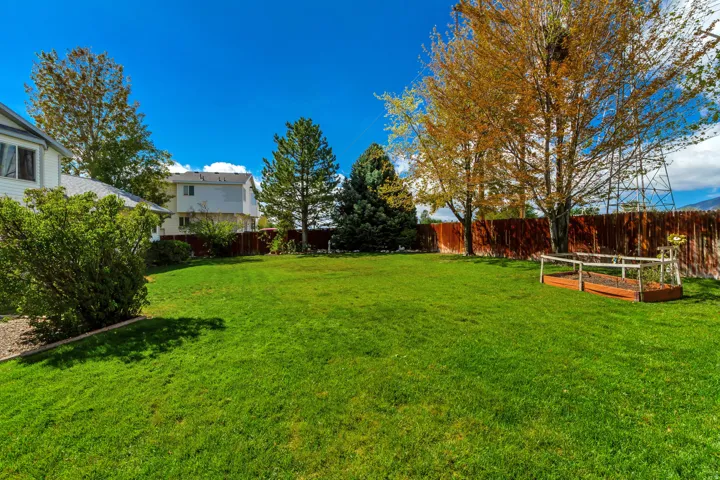 Expansive green lawn with mature trees, established shrubbery, and a raised garden bed