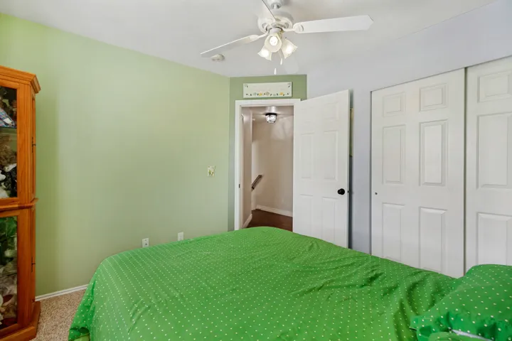 Spacious bedroom with soft sage green walls, carpeted flooring, and ceiling fan with integrated lighting