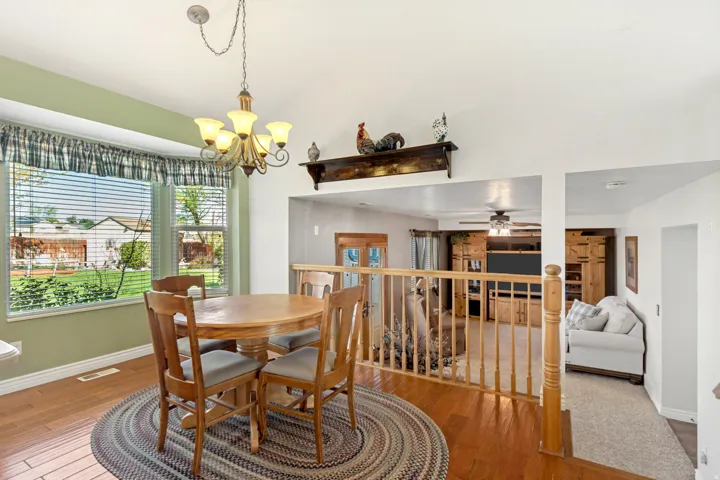 Vaulted ceiling with an overhead chandelier, wood-finish flooring, and a bay window