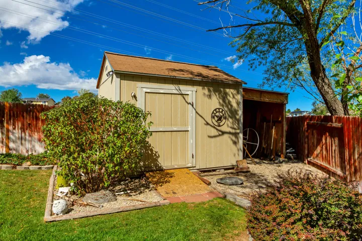 Detached storage shed with a gabled roof and an attached open storage area, bordered by a wood fence