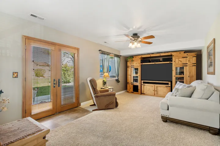 Carpeted living space with a ceiling fan, a window with blinds, and double glass-paneled doors