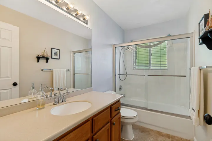 Wood-finish vanity with an integrated sink, polished chrome faucet, and a wall-mounted glass shower enclosure with a tub