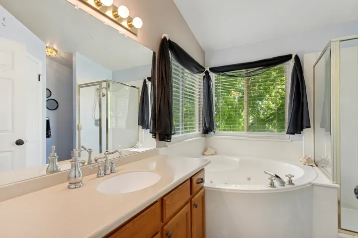Integrated soaking tub with chrome fixtures, glass-enclosed shower, wood-finish vanity with an integrated sink, and a large mirror with a four-light fixture